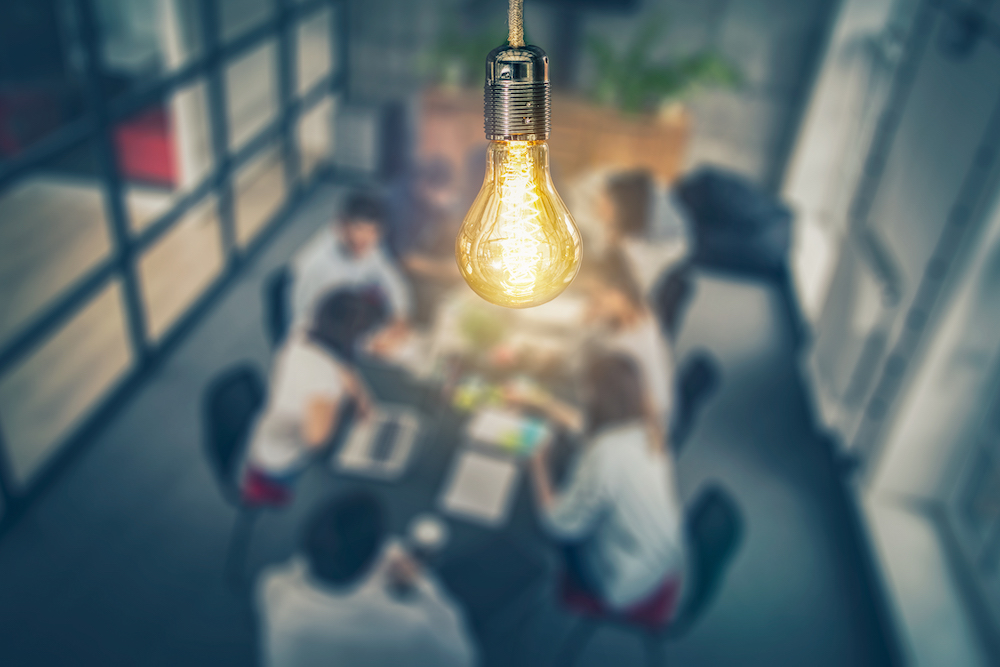 A close-up of a lightbulb over a meeting
