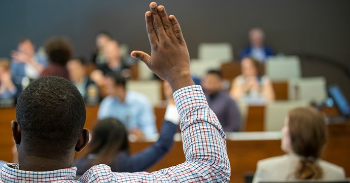 A Black male student raising his hand in class