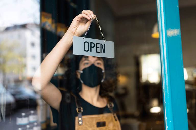 Woman wearing mask placing "open" sign on storefront