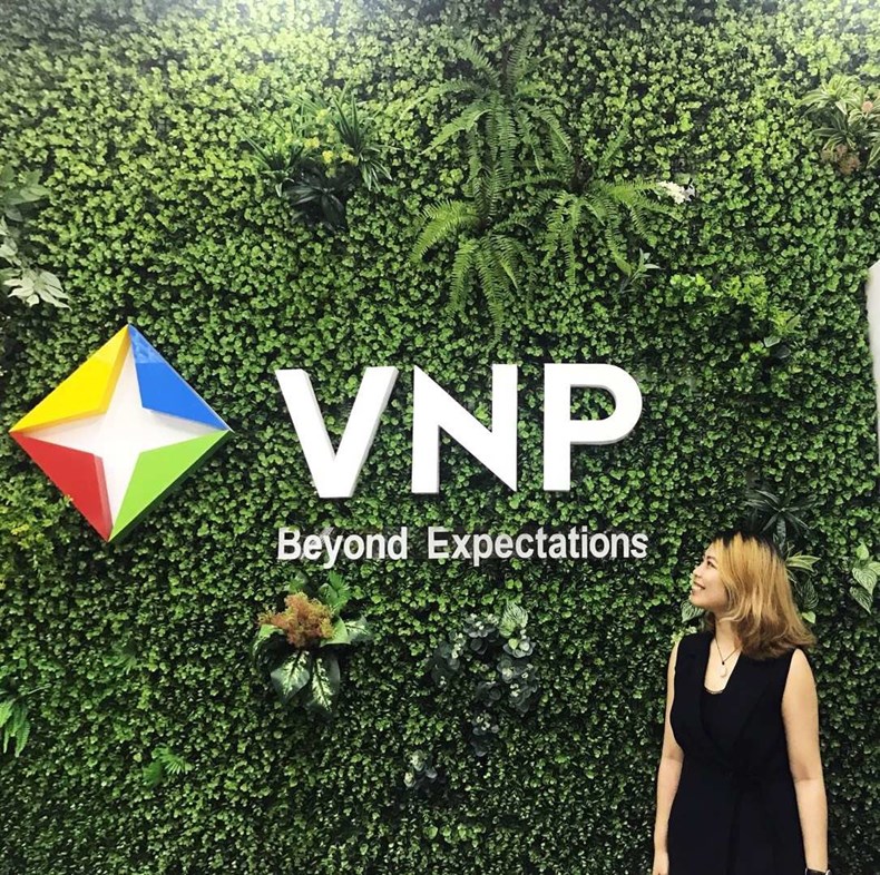 Xiaojun Zhu standing beside the VNP logo