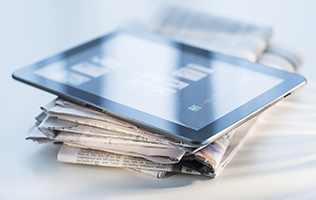 An iPad sitting on a stack of newspapers