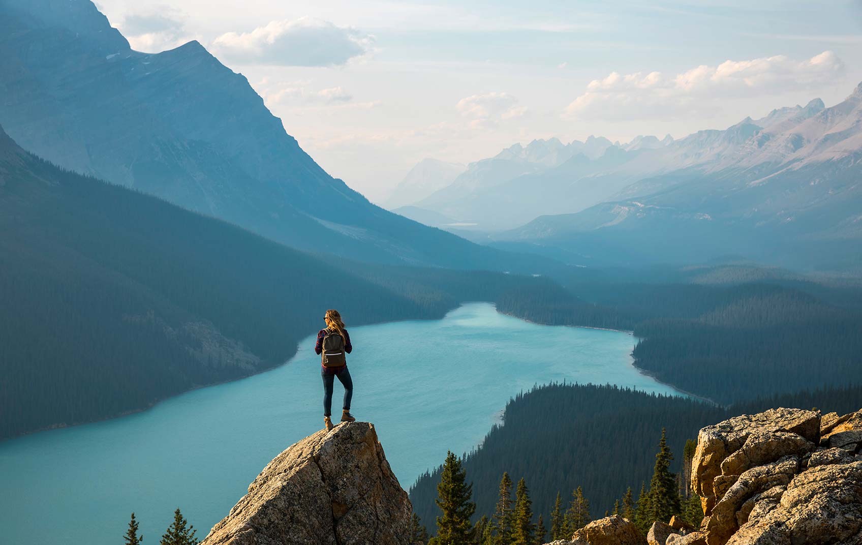 A hiker perched atop a mountain range overlooking a lake