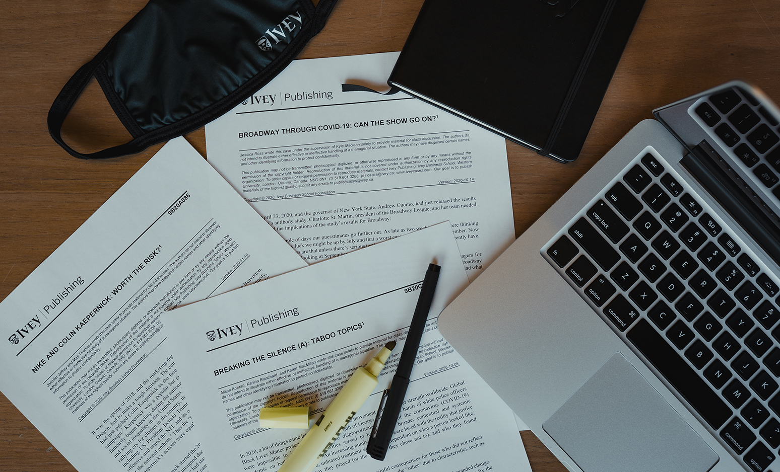 Three cases, a laptop, a book, a pen, a highlighter marker, and an Ivey-branded mask lying on a table