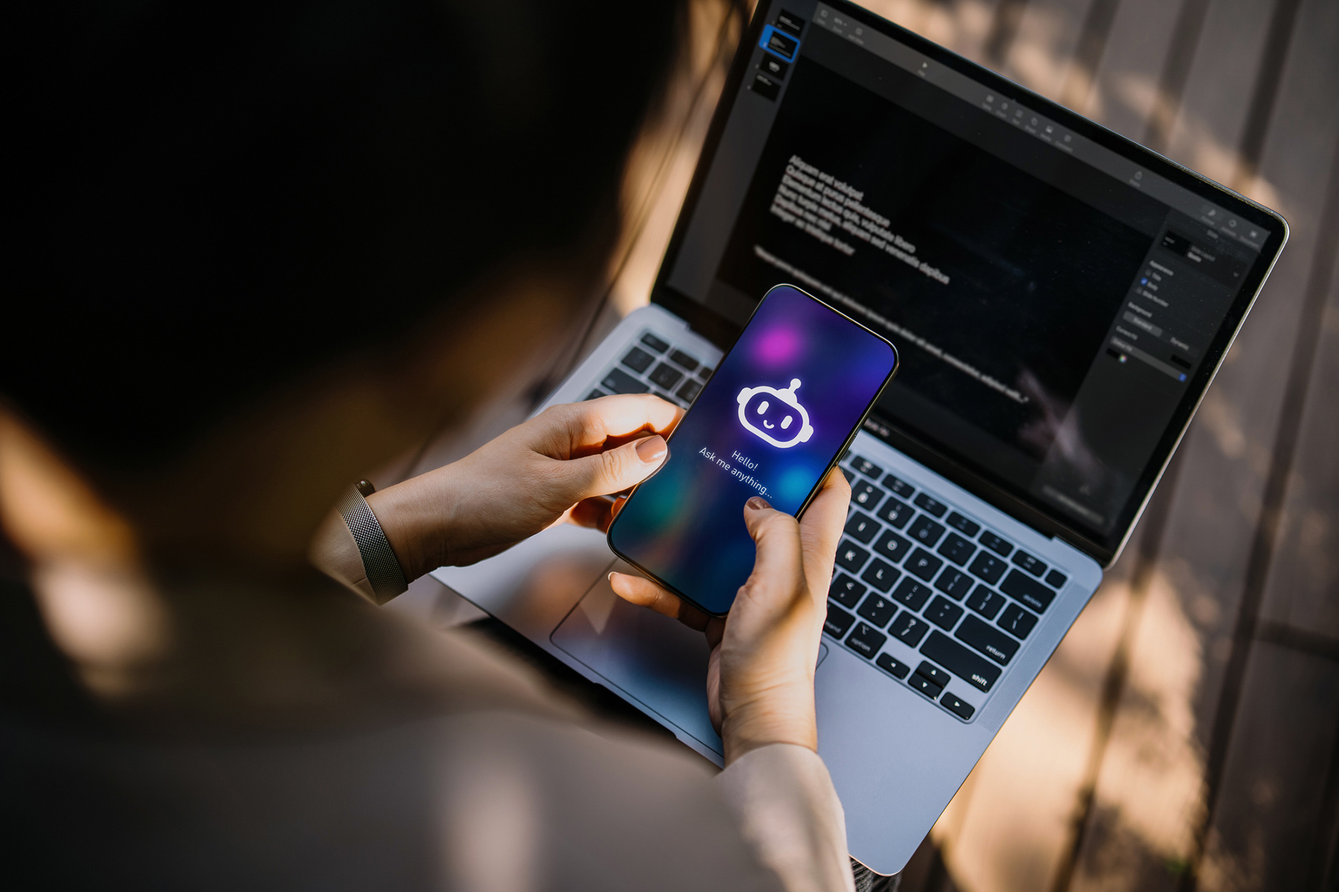 Businesswoman using Chatting AI chatbot virtual assistance app on smartphone to assist her while working on laptop in office park