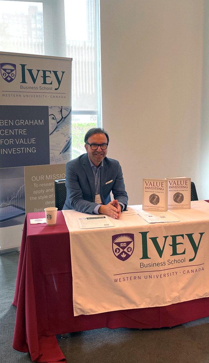 George Athanassakos sitting at the Ben Graham Centre's Booth at the CFA New York's Conference