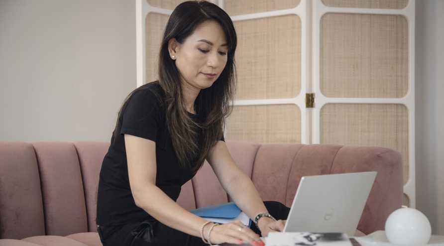 A woman sitting on a couch and typing on a laptop