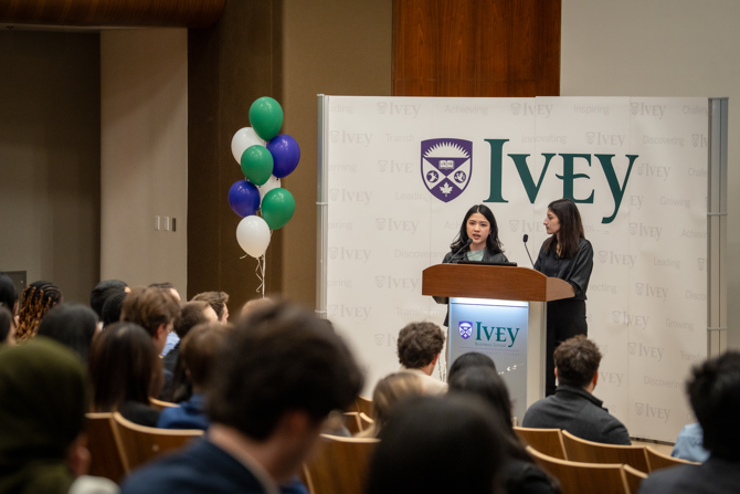 2 students standing at the podium addressing the auditorium of high school students