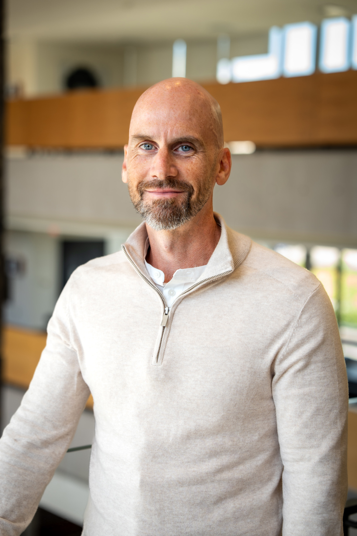 James Kruck, Manager, Applied Research, standing front-facing in focus with the Ivey main foyer slightly out of focus behind him.